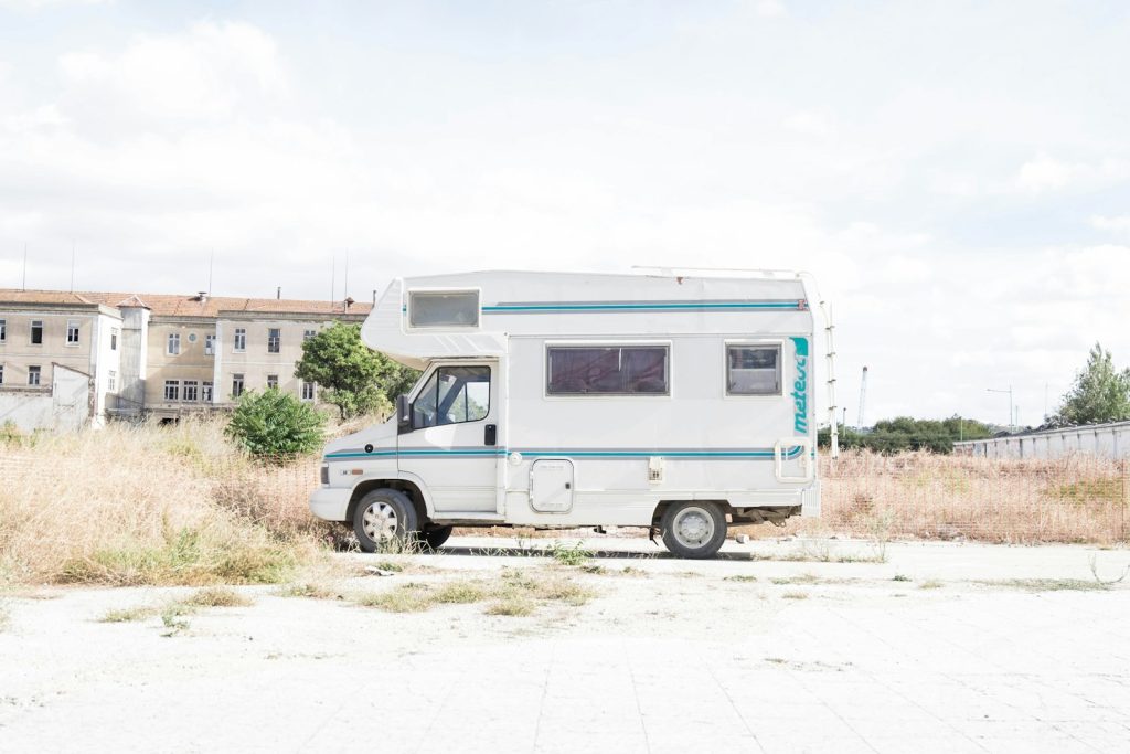White camper van parked in an open area next to a deserted building under a cloudy sky
