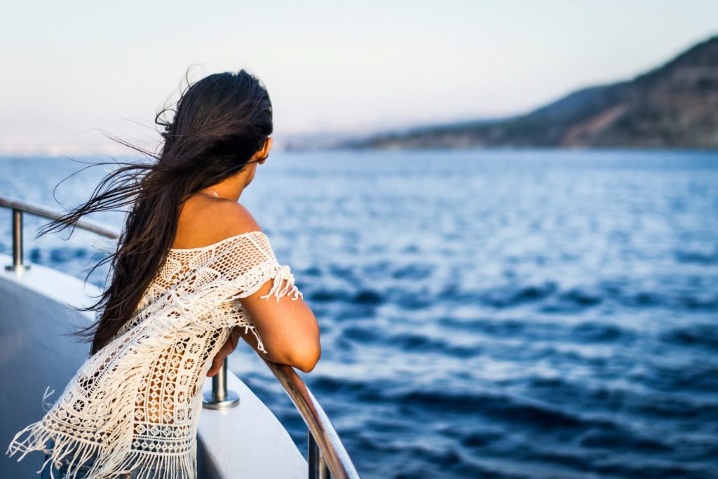 Woman with long hair gazes at the ocean from a boat, wearing a crochet top, enjoying a peaceful sea view